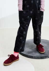 Salopette en denim noir avec des pois gris, grandes poches avant, assortie à des baskets en daim bordeaux et des chaussettes rayées roses.