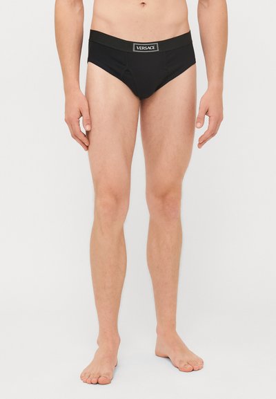 Schwarze Herrenunterhosen mit breitem elastischem Bund, der das Versace-Logo trägt. Der Stoff ist glatt, eng anliegend und minimalistisch im Design.