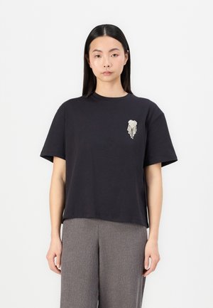 Black cotton t-shirt with a relaxed fit, featuring a decorative embellishment on the left chest. Short sleeves and crew neck design.