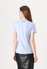 Světle modré tričko s krátkým rukávem a kulatým výstřihem. Na zadní straně se nachází malé černé logo "Karl Lagerfeld". Hladká bavlněná textura.