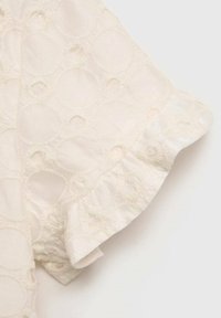 Tessuto bianco con motivi di ricamo circolari, caratterizzato da un orlo arricciato. La texture appare morbida e leggera.