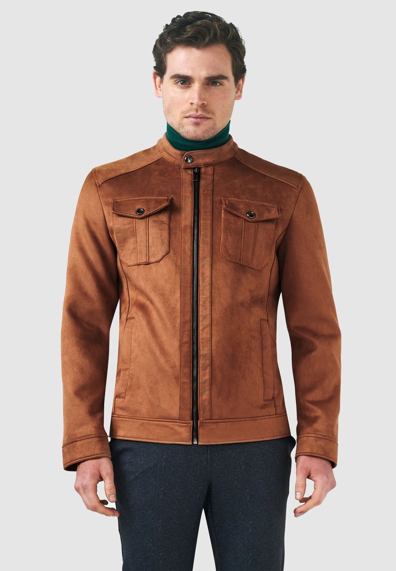 Brun mockakjol med två bröstfickor med lock och knappar, en dragkedja fram och en ståkrage. Texturerad yta.