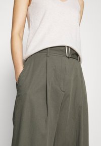 Olive green wide-leg pants made of lightweight fabric, featuring a flat front, two side pockets, and a silver metal buckle on the belt.