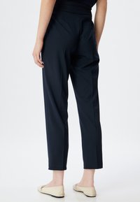 Pantalones ajustados azul marino, con un corte slim, que presentan una cintura alta y perneras rectas; textura suave y largo hasta los tobillos.
