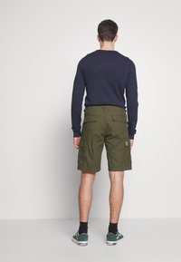 Pantalones cortos cargo verde oliva con dos bolsillos laterales, bolsillos traseros con solapa y cinturilla. Combinados con una camiseta de manga larga azul oscura y zapatillas.