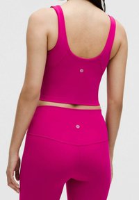 Dopasowany zestaw sportowy z biustonoszem i legginsami w jaskrawym różowym kolorze. Gładka tekstura z krótkim krojem, z logo na plecach.
