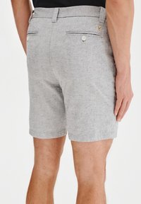 Szare lniane szorty o teksturowanym wykończeniu, z płaskim przodem, dwiema tylkimi kieszeniami z guzikami oraz małym akcentem z tkaniny w pobliżu pasa.