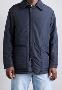 Navyblå isolerad jacka med spetsig krage, dragkedjestängning och två framfickor. Slät yta med sömnadsdetaljer längs framsidan.