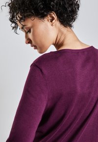 Lila gestrickter Pullover mit Rundhalsausschnitt, der eine weiche Textur und eine lockere Passform aufweist. Sichtbare Schulternaht und sanft fallender Stoff.