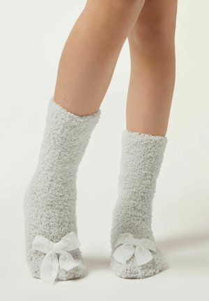 Grå fuzzy sokker med en blød tekstur, længde til midt på læggen og hvide satinbånd ved anklen. Blødt, varmt design for komfort.