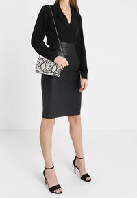 Blusa nera a maniche lunghe, gonna a tubino in ecopelle nera aderente e décolleté neri con tacco a stiletto. Accentuata da una borsa con motivo effetto rettile.