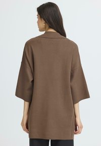 Rudas per didelis džemperis su apykakle, trumpomis rankovėmis ir švelniu paviršiumi. Turi laisvą siluetą ir tiesią juosmens dalį.