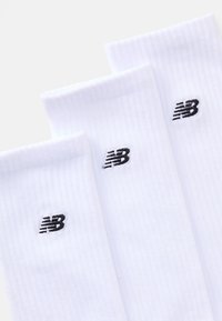 Chaussettes en coton blanches avec une texture côtelée et un logo New Balance noir. Trois paires exposées, présentant un design simple et classique.