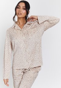 Conjunto de pijama beige con un patrón de leopardo, camisa de botón con cuello y mangas largas; textura de tela suave.