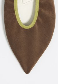 Zapato de ante marrón con punta afilada, con un ribete elástico verde lima alrededor de la abertura. Textura suave con forro blando.