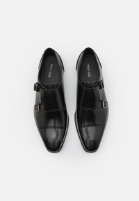 Schwarze Lederschuhe mit einer spitzen Zehe und glatter Textur, die auf der Seite eine Schnalle und ein glänzendes Vorderteil aufweisen.