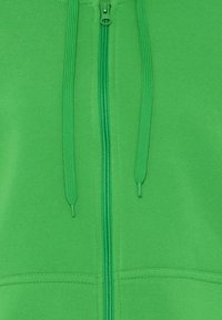 Zelená mikina na zip s hladkou texturou látky, nastavitelné šňůrky, centrální zip a jemné detaily švů.