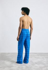 Blauwe geruite pyjamabroek met een elastische tailleband, met een losse pasvorm en een zachte textuur, getoond op een model van achteren.