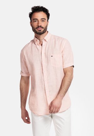 Chemise boutonnière à manches courtes rose clair avec une poche poitrine. Fabriquée en tissu texturé avec une coupe décontractée, portée sur un pantalon blanc.