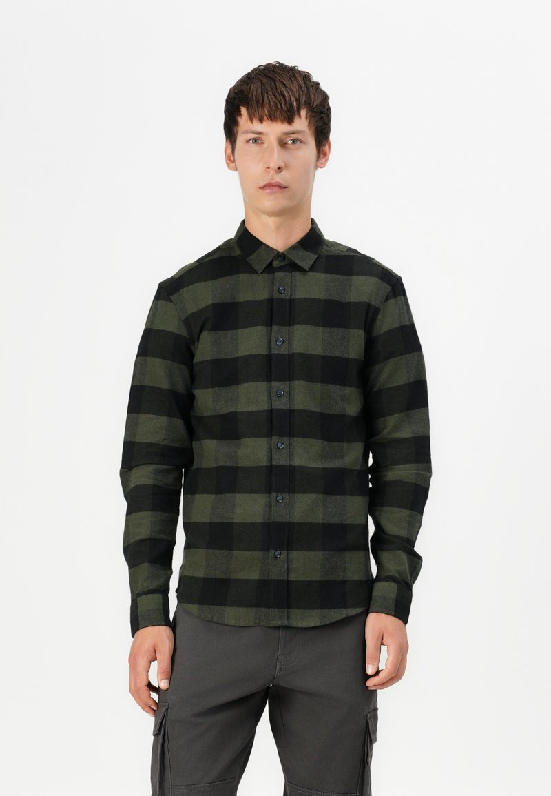 Groene en zwarte geruite overhemd met lange mouwen, knoopsluiting aan de voorkant, kraag en textuurstof. Model draagt een grijze cargo broek.