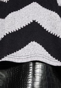 Tissu à motif zigzag noir et gris avec une texture lisse, superposé sur un matériau en similicuir noir brillant imitation crocodile.