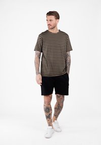 Camiseta de manga corta a rayas en verde oliva combinada con pantalones cortos cargo negros, llevada con zapatillas deportivas blancas. Presenta un corte holgado y una textura suave.