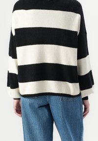 Gestrickter Pullover mit schwarz-weißen horizontalen Streifen, der eine lockere Passform, weite Ärmel und eine gerippte Textur aufweist. Kombiniert mit hellblauen Jeans.