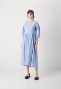 Blå og hvit stripete kjole til kneet med pufferm, rund halsutskjæring og rynket midje. Brukt med svarte loafers med hardware-detaljer.