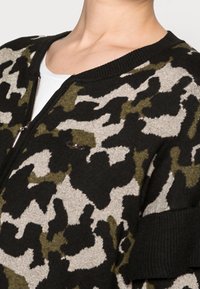 Cardigan con estampado camuflaje en tonos verdes, negros y beige; cuenta con cierre frontal de cremallera, cuello de canalé y textura de punto suave.