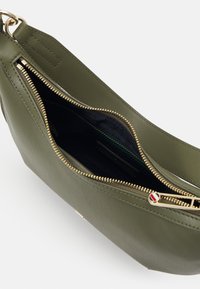Sac à main en cuir vert olive avec une fermeture éclair dorée partiellement ouverte, révélant un intérieur en tissu foncé et une tirette zippée rayée.