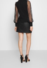 Svart långärmad topp med genomskinliga puffärmar, i kombination med en svart läderminikjol och klackskor med ankelsnor och träklackar.