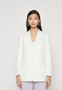 Blazer bianco a righe con rever a coscia, due tasche frontali e chiusura con bottoni. Tessuto liscio e vestibilità su misura.