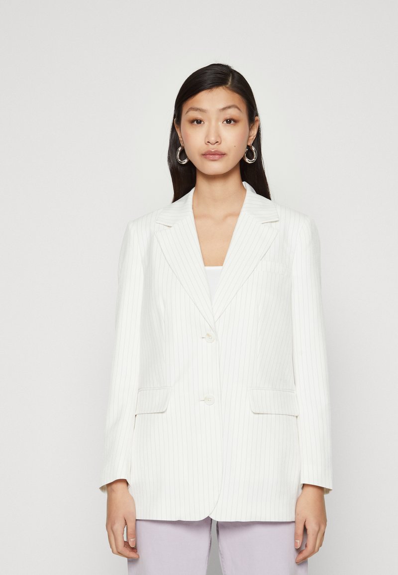 Blazer bianco a righe con rever a coscia, due tasche frontali e chiusura con bottoni. Tessuto liscio e vestibilità su misura.