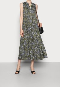 Vestido sin mangas verde con patrón floral en blanco y negro, con botonera en el escote, falda acampanada, combinado con sandalias negras de tiras y bolsa de hombro.