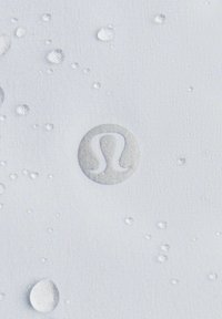 Water-resistant fabric in light gray featuring silver logo and small water droplets. Textured surface with smooth, matte finish.