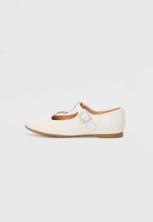 White flat shoe with a rounded toe, cutout design, buckle accent, and a low profile. Made of smooth synthetic material with a beige sole.