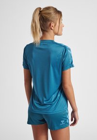Aktivklesett i teal: kortermet topp og shorts, glatt tekstur, lett materiale, med merkevarelogo og kontrastfarger på skuldrene.
