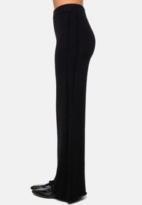 Pantalons en tricot noirs à taille haute avec un détail en tricot en câble sur le côté, présentant un design à jambe droite et portés avec des chaussures noires plates.