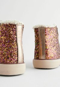 Bottines scintillantes roses et dorées avec une doublure blanche duveteuse, présentant une surface texturée et des panneaux latéraux métalliques lisses. Semelles en caoutchouc.