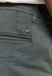 Groene stoffen broek met een achterzak voorzien van een hexagonaal zwart hardware accent en subtiele oranje strepen. Vlakke textuur en een op maat gemaakt ontwerp.