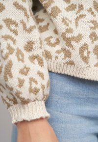 Maglione lavorato a maglia beige e bianco con motivo a stampa leopardata, caratterizzato da polsini arricciati e orlo a costine, abbinato a denim azzurro chiaro.