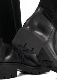 Black leather ankle boots feature a thick, textured rubber sole, smooth finish, and zipper detail on the side for easy wear.
