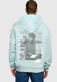 Lyseblå hoodie med et stort grafisk tryk på ryggen, der viser sort-hvide billeder, teksten "ZAYN" og geometriske accenter. Fremstillet af bomuldsmateriale.