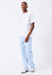 Hvid kortærmet t-shirt parret med lyseblå brede bukser. Bukserne har en afslappet pasform og subtile syninger. Sorte og hvide sneakers fuldender outfittet.