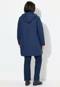 Giacca impermeabile blu navy con cappuccio, maniche lunghe e taglio dritto. Presenta una texture liscia e un design pratico con tasche laterali.