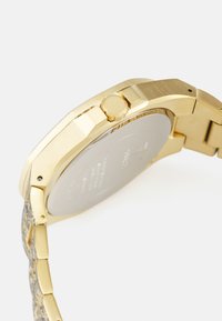 Gold-tone wristwatch with a stainless steel case, textured bracelet, and a prominent crown. Smooth, polished finish on the case back.