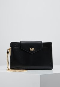 Černá kožená kabelka se zlatým řetízkem, ozdobená klopou a embosovaným logem. Hladký povrch a ostrý design.