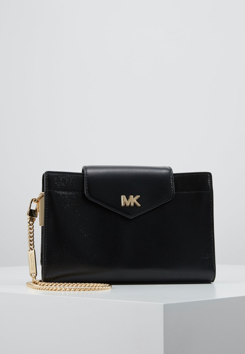 Černá kožená kabelka se zlatým řetízkem, ozdobená klopou a embosovaným logem. Hladký povrch a ostrý design.