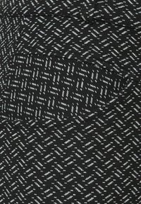 Svart tyg med ett geometriskt mönster i ljusgrått, med en texturerad yta och en synlig fickdetalj.