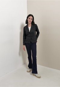 Zwarte pinstripe blazer met twee knopen, gecombineerd met flared donkere broeken. Het model draagt een witte top en lichte sneakers. Eenvoudig, gestructureerd ontwerp.